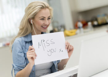 Woman video chatting at home using a laptop and holding a miss you sign